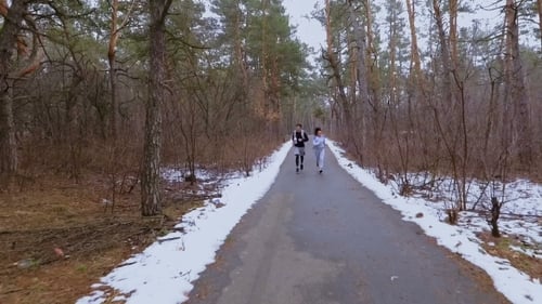 Two Young Friends Runs Along the Road in Winter Forest