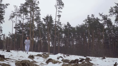 Young Beautiful Brunette Wears Sportswear Is Running in the Snow Forest
