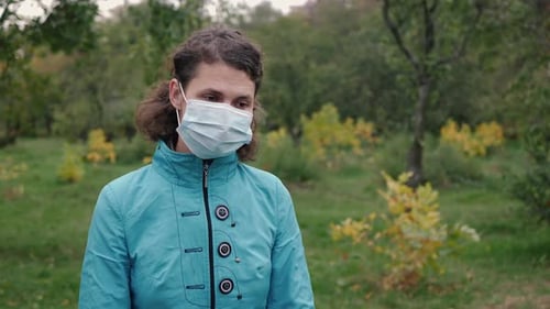 Woman Puts on Surgical Mask in Park