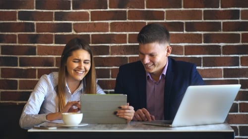Two Laughing Coworkers Discussing Work Project While on Lunch Break in Cafeteria