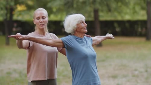 Senior Woman Stretching With Trainer in Park