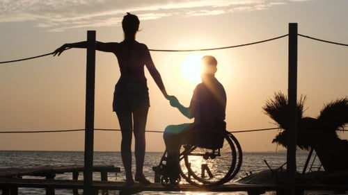Girl with Friend Handicapped Holding Hands Stand on Pier and Look at Sunset