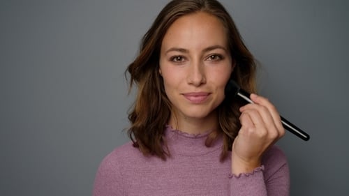Woman Applies Makeup with Brush in Close Up