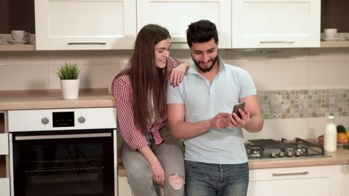 Happy Couple Looking at Smartphone in Kitchen