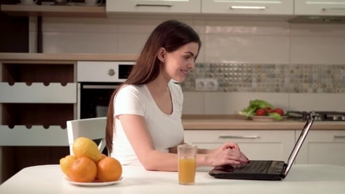 Smiling Woman Typing at Kitchen Table With Laptop