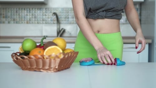Woman Measures Waist with Fruits in Kitchen
