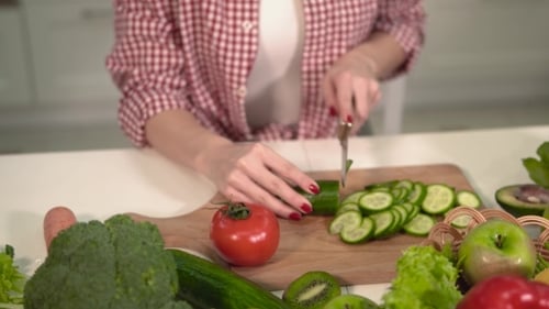 Woman Cuts Cucumber in Kitchen Surrounded by Produce