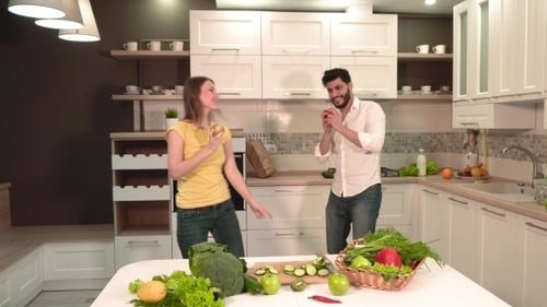 Playful Couple Dancing with Vegetables in Bright Kitchen