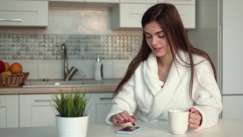 Woman in Robe Drinking Coffee and Using Phone
