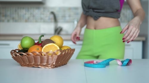 Woman Measures Waist Next to Fruit Basket