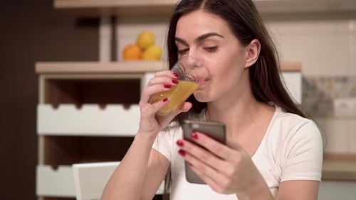 Smiling Woman Using Smartphone and Drinking Juice Indoors