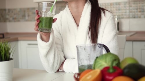 Young Woman Drinks Healthy Green Smoothie in Kitchen