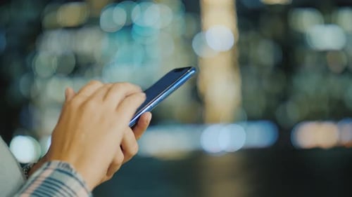 Man's Hands with Smartphone on Bokeh Background From City Lights