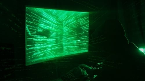 A Man Hacker in a Hood in a Dark Room Works with the Program Code