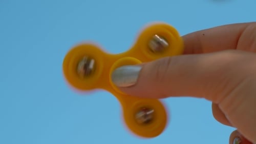 Hand Spins Yellow Fidget Spinner Against Blue Sky