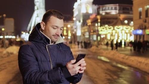 Young Man Uses Phone at Night City Background