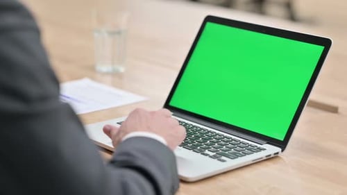 Person Typing on Laptop with Green Screen Display