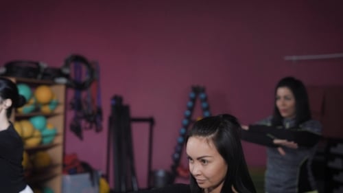 Kräftiges Mädchen engagiert sich in einem Fitnessraum in einer Gruppe, lächelt, bewegt sich die Hände, hockt und dreht sich