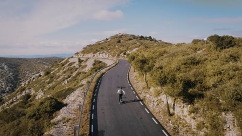 Hipster Man Rides on Skateboard on Mountain Road