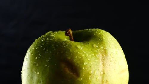 Green Apple with Water Drops Rotates on Black Background