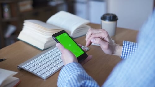 Homem está segurando smartphone com tela verde no café