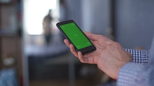 Mann hält Smartphone mit Greenscreen im Café
