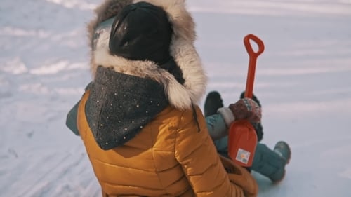 Young Mother and Little Daughter Having Fun on Sledge in Winter Park