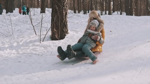 Junge Mutter und kleine Tochter haben Spaß auf dem Schlitten im Winterpark