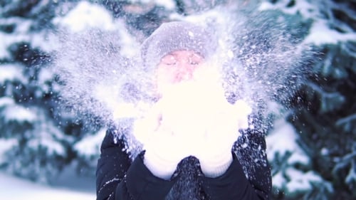 Girl Blowing Snow in a Winter Park, Smiling and Enjoying the Snow