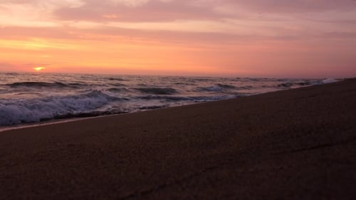 Sandy Beach and Beautiful Waves Forming the Foam in the Beams Sunset
