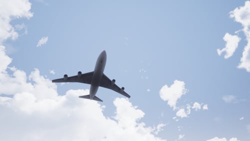 Passenger Airplane Flying Overhead Through Blue Sky With Clouds