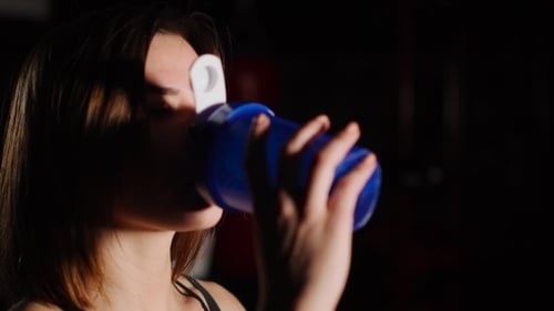 Gorgeous Young Woman with a Towel on Her Neck Drinking Water From a Bottle at the Gym.