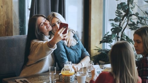 Two Beautiful Girls Are Doing Selfie in a Cafe and Smiling