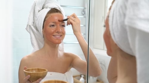Young Woman with a White Towel Put on Her Face a Brown Moisturizing Mask
