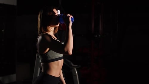 Gorgeous Young Woman with a Towel on Her Neck Drinking Water From a Bottle at the Gym
