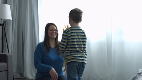 Boy Gives Flowers to Mother, Hug in Bright Room