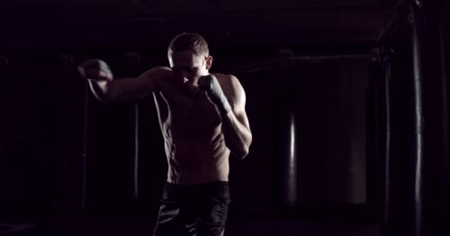Male Boxer Practicing in a Dark Boxing Gym