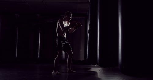 Man Boxing on Punching Bag in Dark Gym