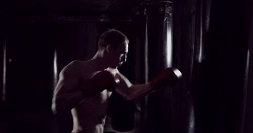 Man Boxing with Punching Bag in Dark Gym