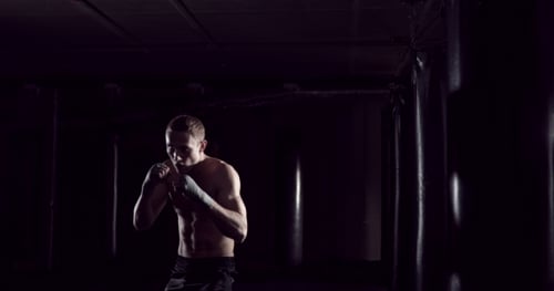 Intense Boxer Training in Dark Gym with Punching Bags