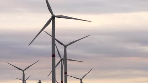 Motion the Blades of a Large Wind Turbine in a Field Against a Background of Orange Sunset on the