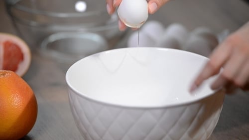 Weibliche Hände brechen ein Ei und trennen Eigelb von Weiß