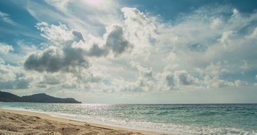 Strand und Berge dahinter. Aus den Wolken bahnen sich Sonnenstrahlen