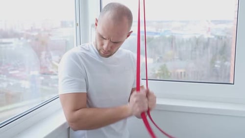 A Young Athletic Man Exercises with Elastic Bands at Home