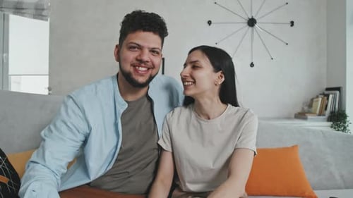 Cheerful Couple Waving and Talking to Camera at Home