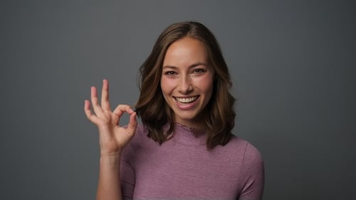Smiling Woman Gives Okay Sign on Grey Background