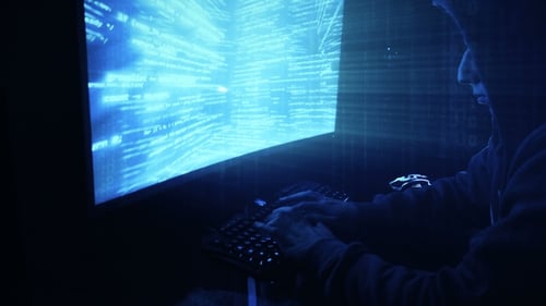 A Man Hacker in a Hood in a Dark Room Works with the Program Code