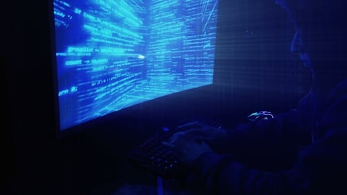 A Man Hacker in a Hood in a Dark Room Works with the Program Code