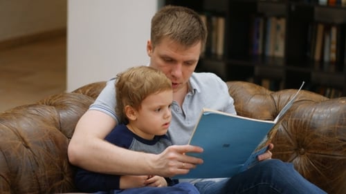 Loving Father Reads Story to Young Son at Home
