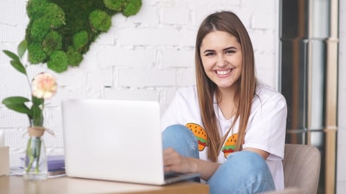 a Young Girl Is a Freelancer Working in the Cafe with a Laptop and Smiling at Camera